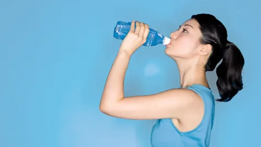 Person drinking bottled water against a blue background, demonstrating hydration for UK emergency preparedness.

